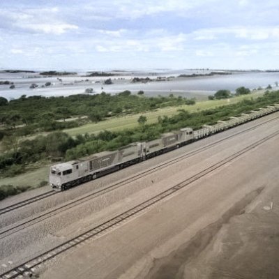 A long train travels on a track with fields and open country either side of it.